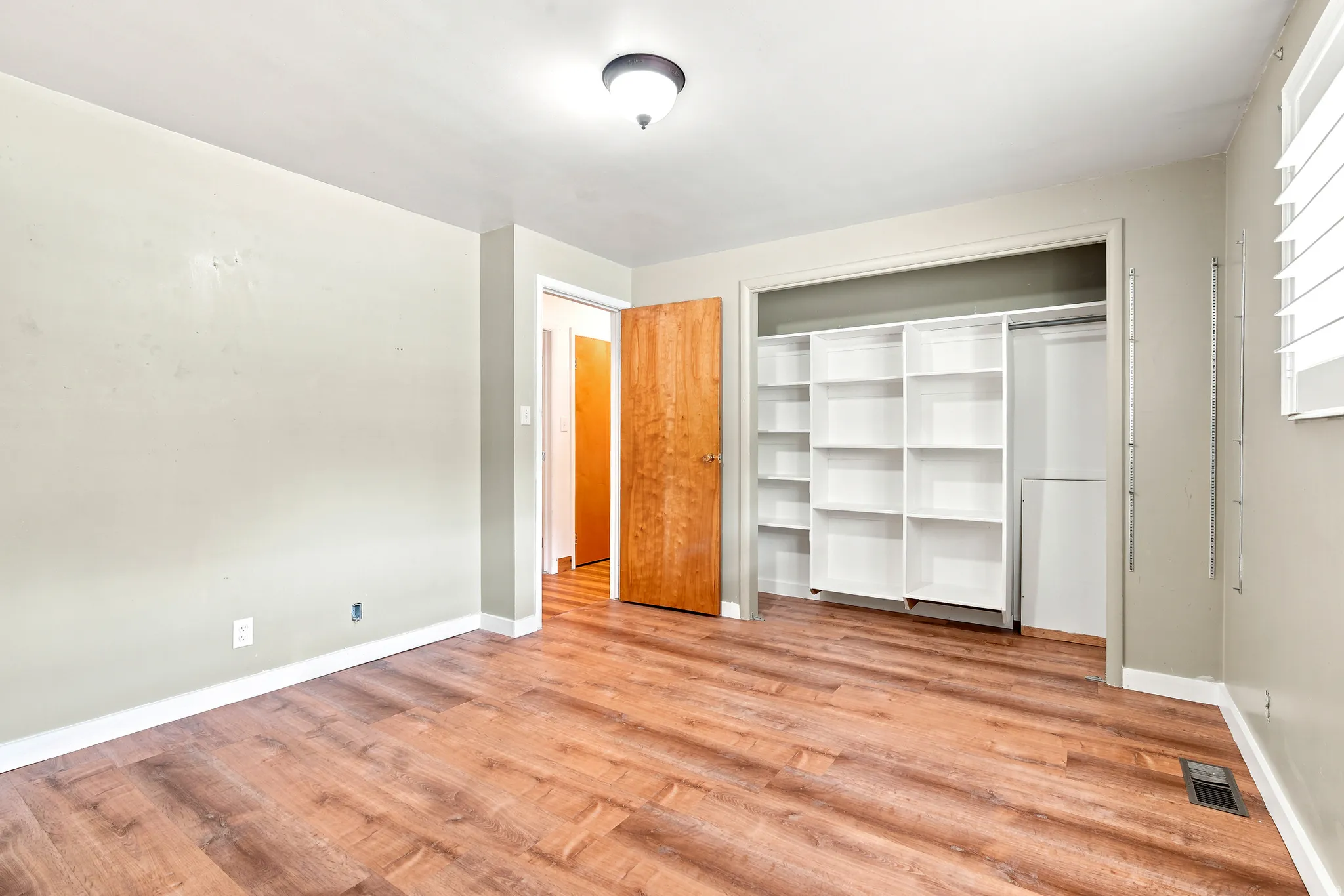Room with wood-finish flooring, light neutral wall paint, and white baseboards