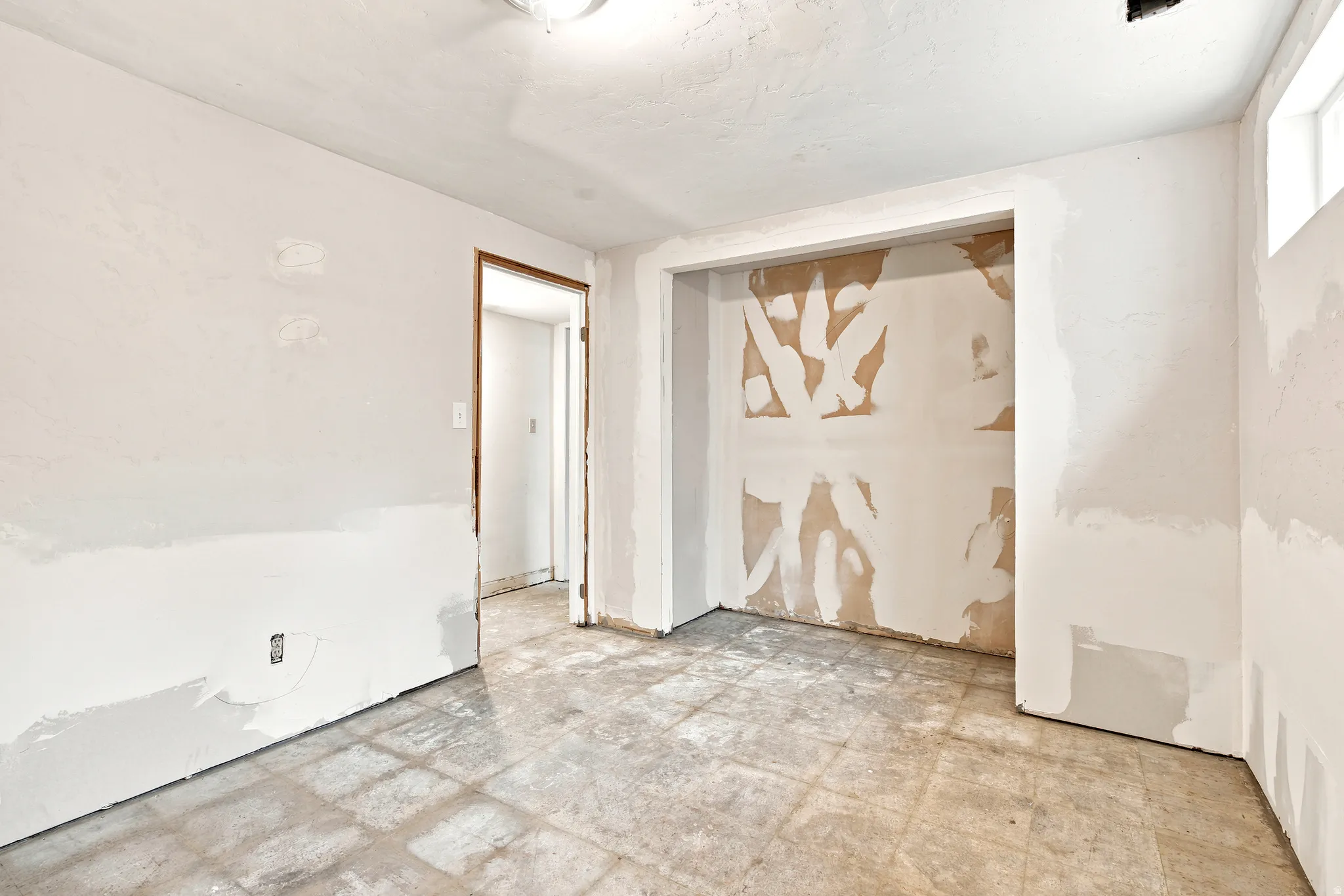 Unfinished interior space featuring light-colored walls, a recessed closet area, a single door frame, and a ceiling-mounted light fixture