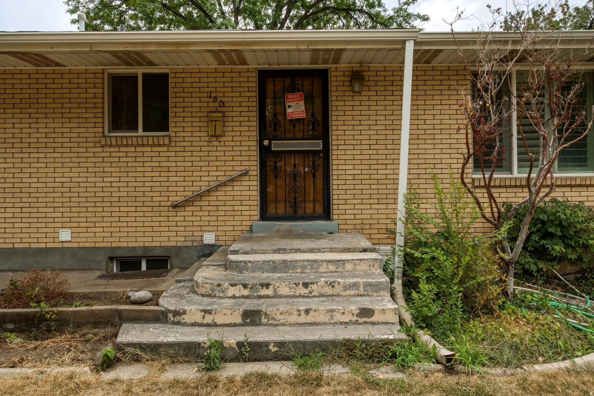 Brick facade exterior featuring a security screen door, concrete entry steps, and a handrail