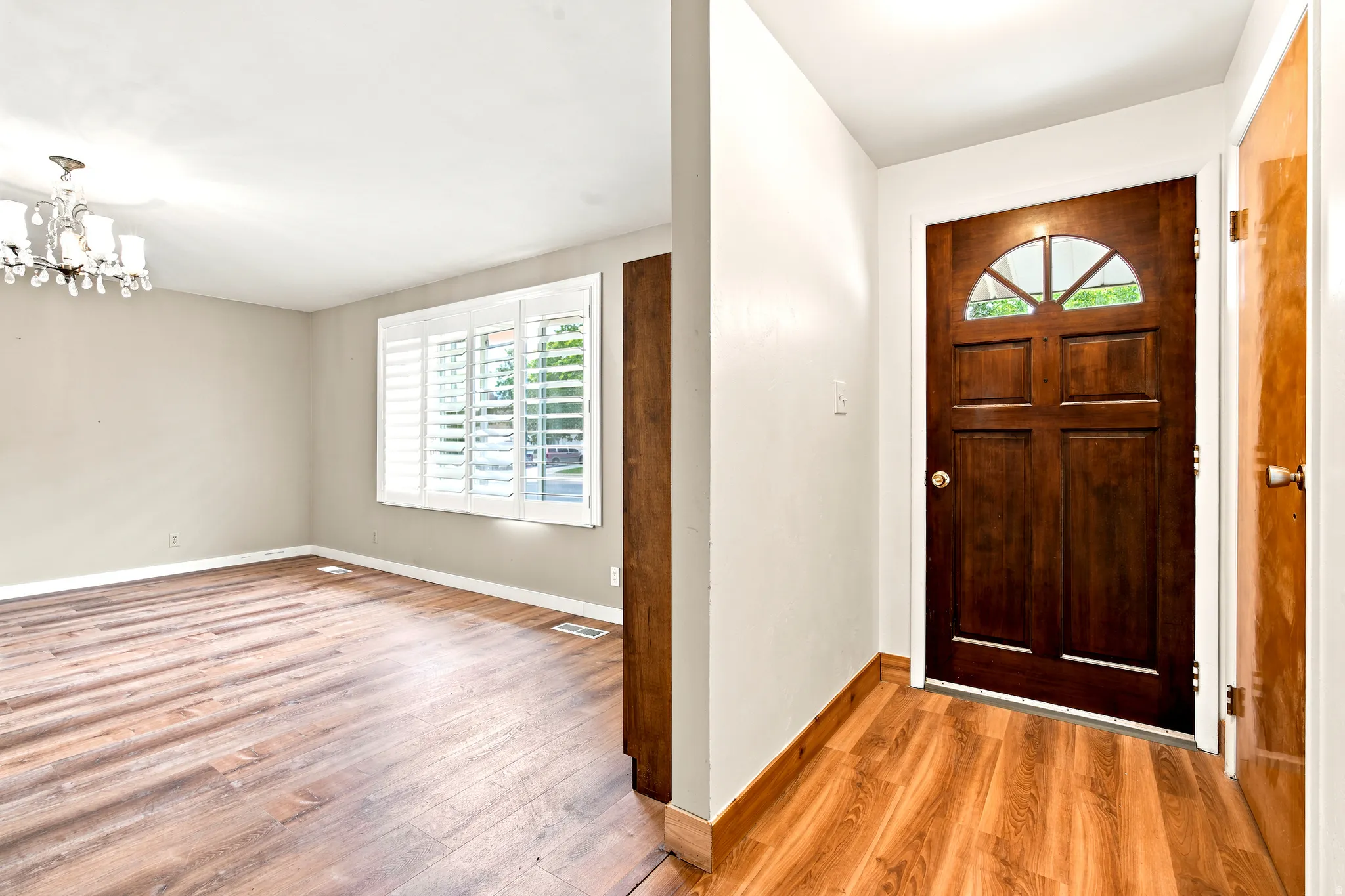 Entryway featuring a rich wood-paneled door with an arched window, wood-finish flooring, and a chandelier lighting fixture