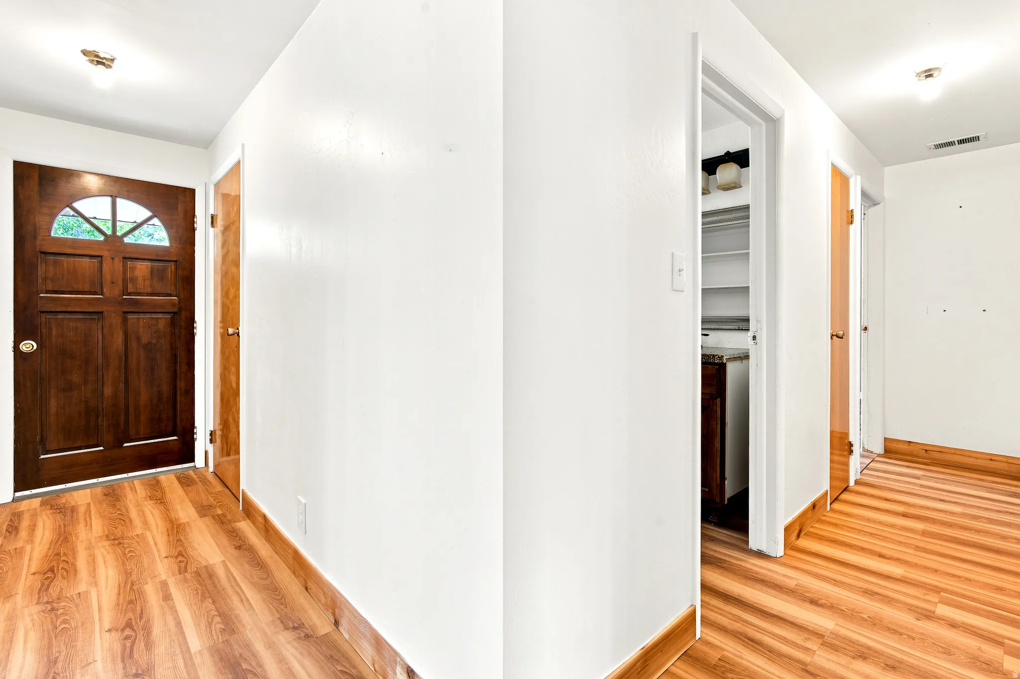 Entryway featuring a paneled wood door with an arched window, wood-finish flooring, and white walls