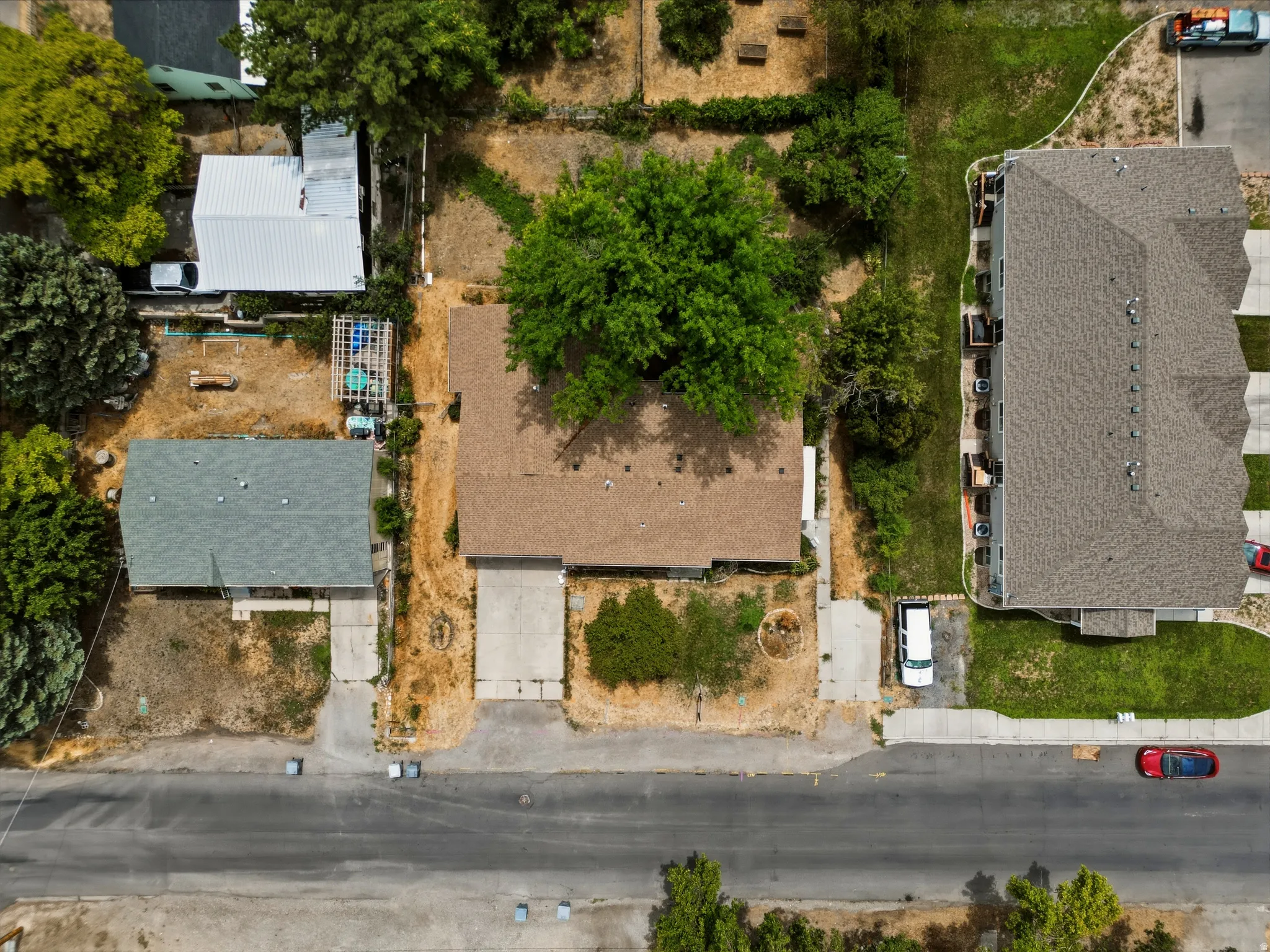 Aerial property overview featuring a main residence with a brown shingle roof, a secondary structure with a gray shingle roof, and a mature tree providing natural shade