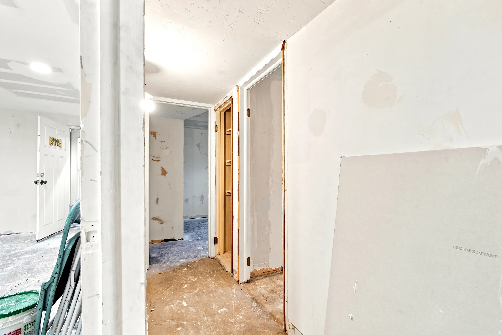 Hallway with exposed drywall, unfinished flooring, and multiple doorways