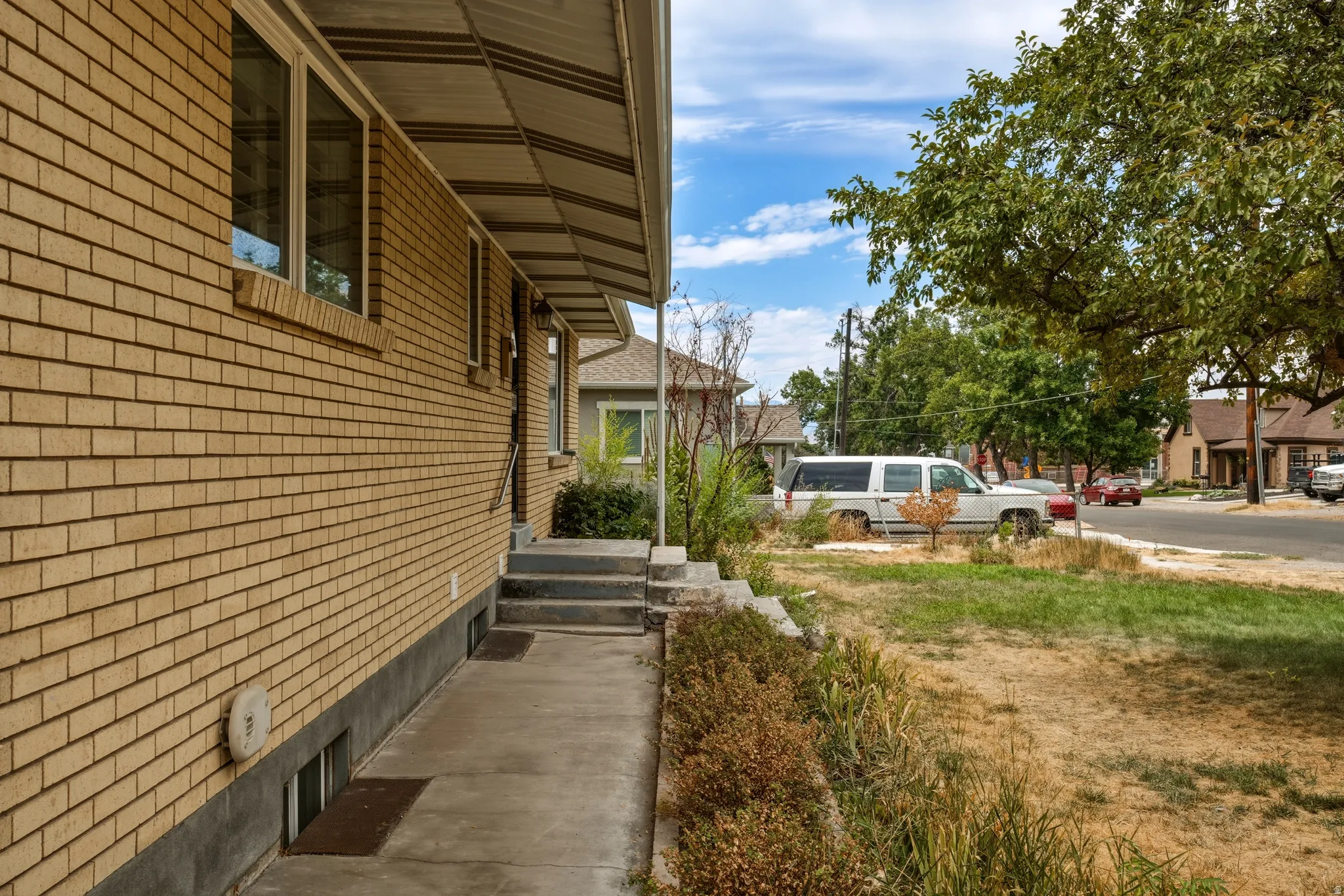 Brick exterior featuring a covered entry, concrete walkway, multiple windows, and partial landscaping