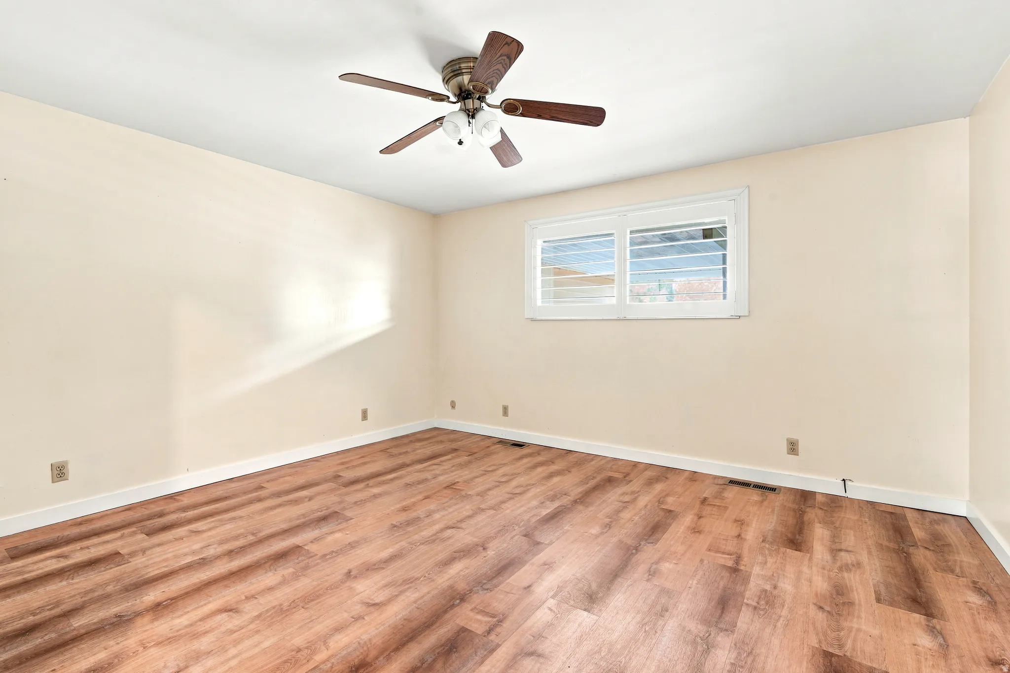 Room featuring wood-finish flooring, light-toned walls, a ceiling fan with integrated lighting, and a window with horizontal blinds