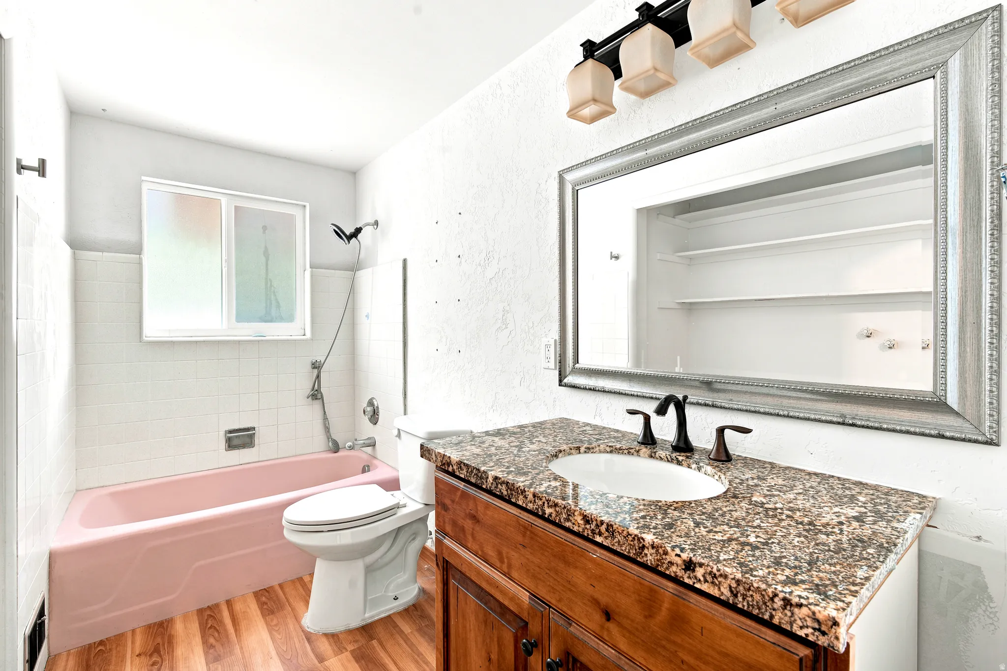 Bathroom featuring a granite countertop vanity with dark wood-finish cabinetry, a framed mirror, and wood-finish flooring