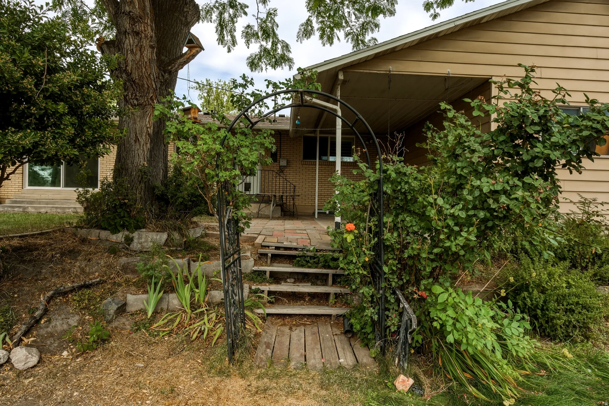 Front entry featuring a decorative metal archway, wooden steps, and a brick patio
