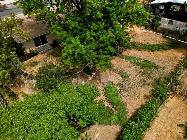 Expansive exterior grounds featuring a large unlandscaped area, established trees, and a terraced retaining wall