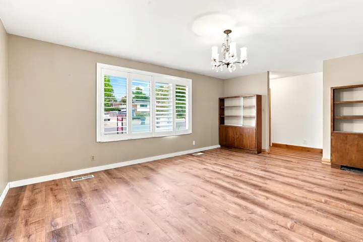 Spacious interior room featuring wood-finish flooring, a window with white plantation shutters, built-in shelving with cabinetry, a second built-in shelving unit, and an overhead chandelier light fixture