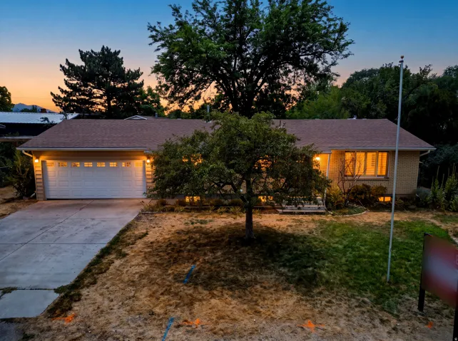 Ranch-style residence featuring a prominent two-car garage with overhead lighting, a paved driveway, and a brick exterior