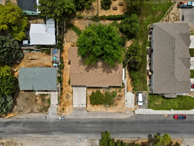 Aerial property overview featuring a main residence with a brown shingle roof, a secondary structure with a gray shingle roof, and a mature tree providing natural shade
