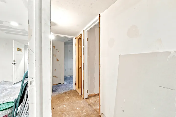 Hallway with exposed drywall, unfinished flooring, and multiple doorways