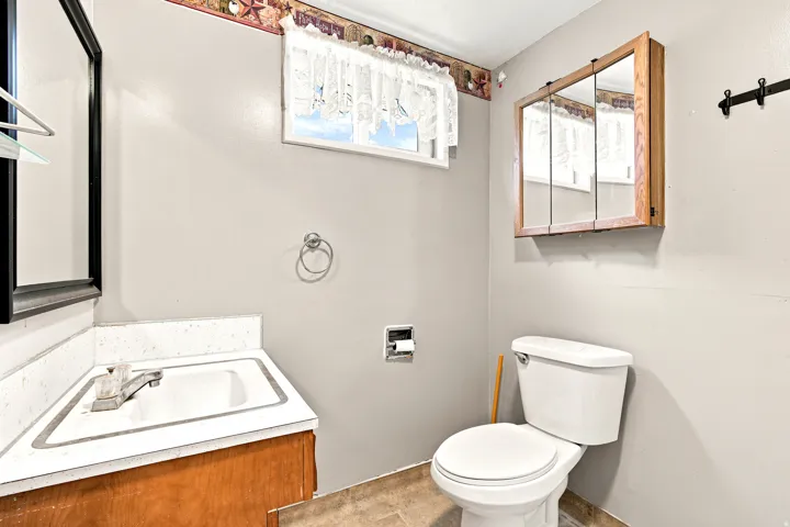 Bathroom featuring a wood-finish vanity with an integrated sink, a wall-mounted medicine cabinet with mirrored doors, and a window with a lace valance