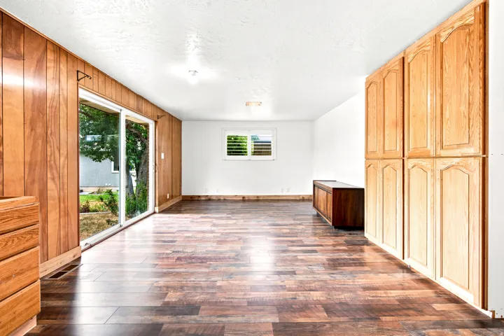 Spacious interior room featuring wood-finish flooring, full-height wood paneling, and an expansive sliding glass door