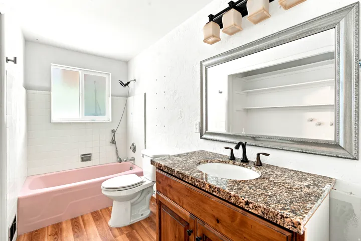Bathroom featuring a granite countertop vanity with dark wood-finish cabinetry, a framed mirror, and wood-finish flooring