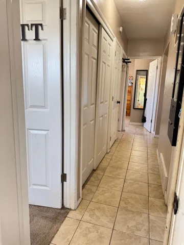 Hallway featuring light-toned tile flooring, white paneled doors, and neutral wall paint