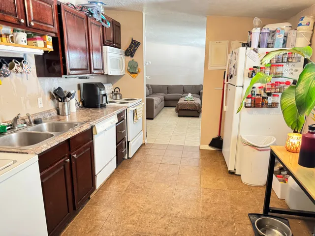 Kitchen featuring dark wood-finish cabinetry, a dual basin stainless steel sink, and white appliances