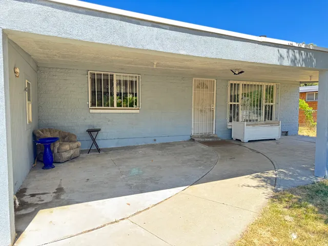 Covered porch entry featuring a light-colored security door, a large window with security bars, and a concrete patio