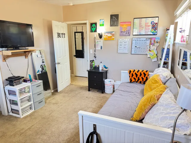 Carpeted room featuring a white door, light beige walls, and a window with blinds
