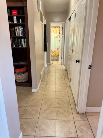 Hallway featuring square tile flooring, neutral wall paint, and white trim
