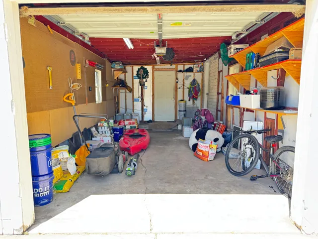 Spacious garage featuring a concrete floor, built-in shelving, exposed ceiling joists, and a rear access door