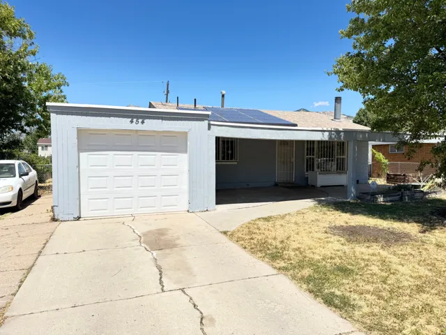 Single-story residence featuring an attached garage with a panel door, a covered entry porch, and solar panels on the roof