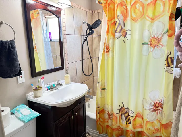 Bathroom featuring a dark wood-framed mirror, vanity with a white basin sink, polished chrome faucet, and tiled shower surround