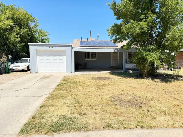 Single-story residence featuring an attached garage with a white panel door, covered carport, and a prominent front yard
