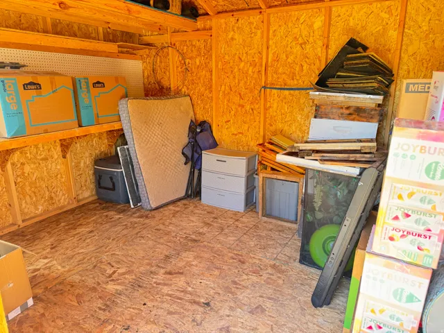 Interior storage shed featuring OSB paneling, exposed wood framing, built-in shelving, and a pegboard storage wall