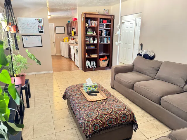 Spacious living area featuring neutral-toned tile flooring, light-colored wall paint, and a built-in dark wood bookcase