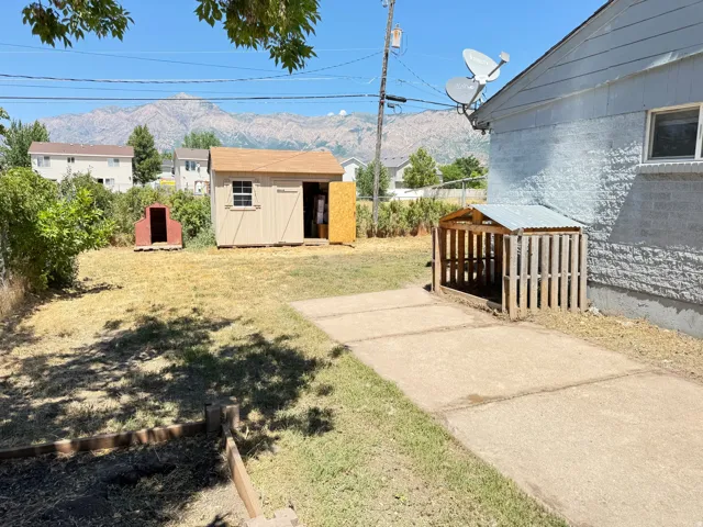 Expansive backyard featuring a storage shed, concrete patio, mountain backdrop, and structural elements