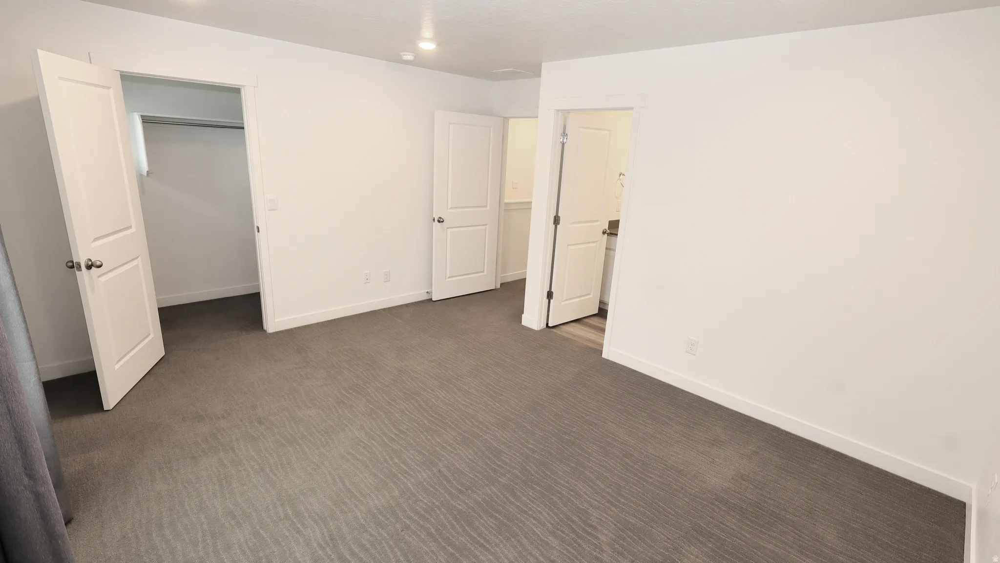 Spacious interior room featuring light-colored walls and patterned carpet flooring