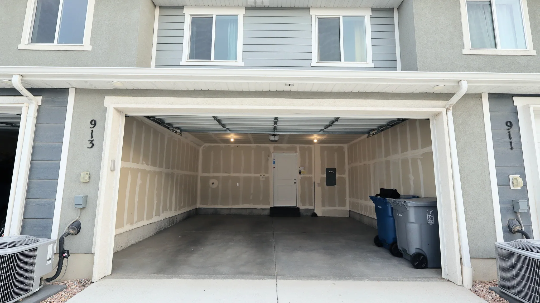 Two-car garage with concrete flooring and exposed drywall, featuring a rear entry door and ceiling-mounted lighting