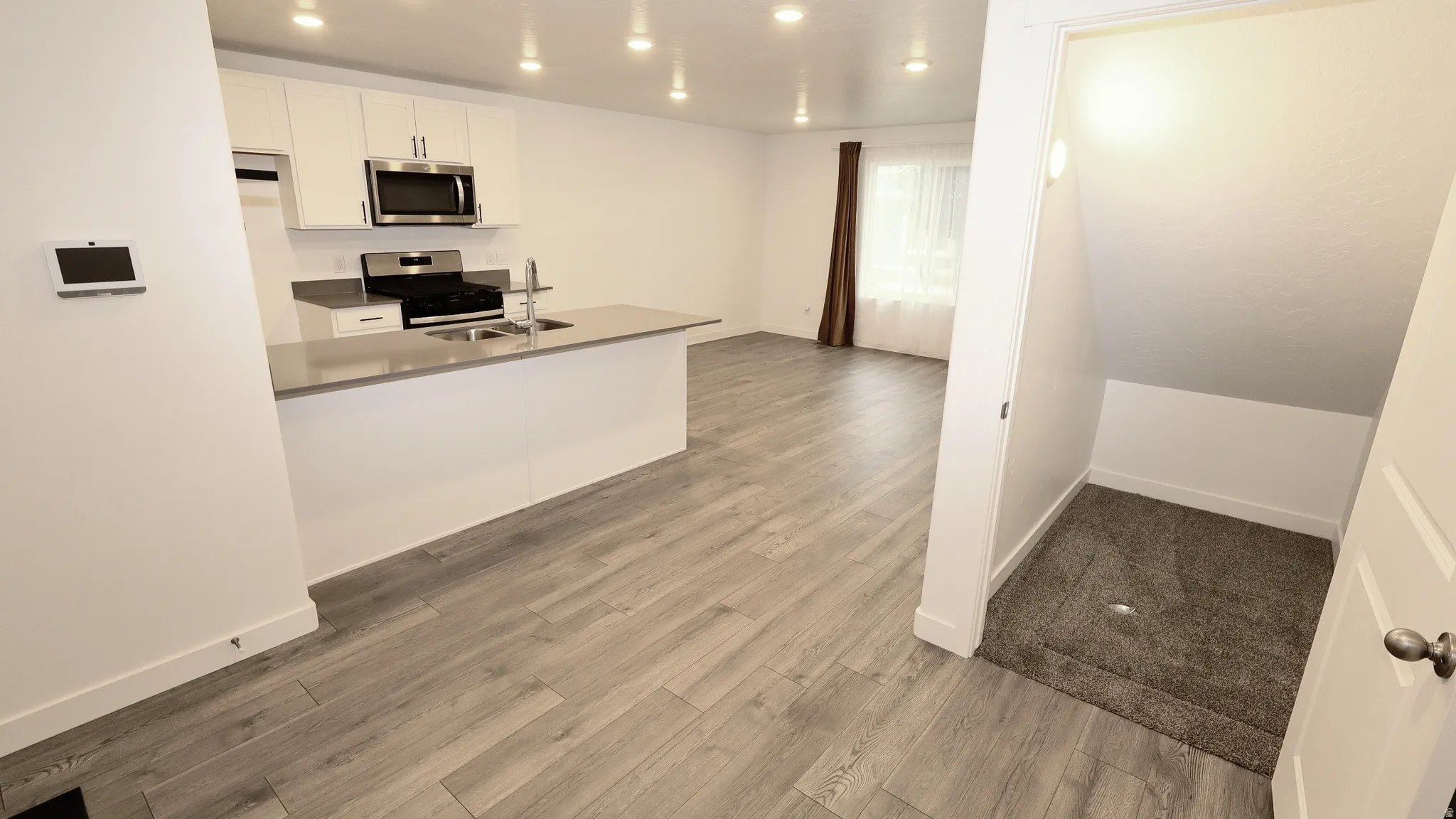 Open-concept living space featuring wood-finish flooring throughout, a modern kitchen with white cabinetry, stainless steel appliances, and a central island with an integrated sink