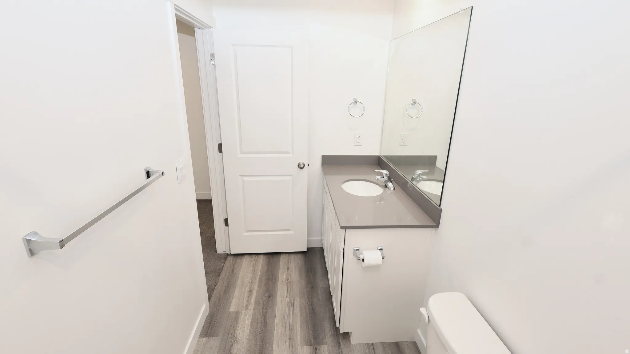 Bathroom featuring wood-finish flooring, a white vanity with a gray countertop, an undermount sink, a large wall-mounted mirror, and white paneled doors