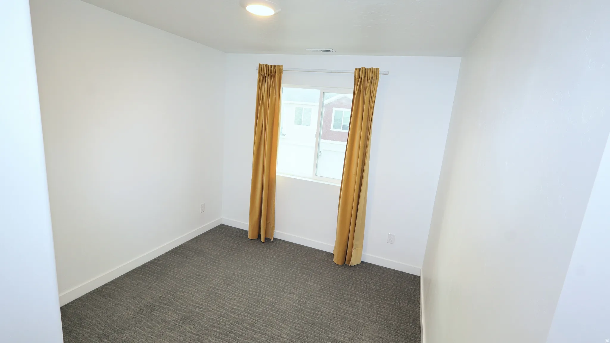 Room featuring white walls, dark patterned carpet, and a flush-mounted ceiling light