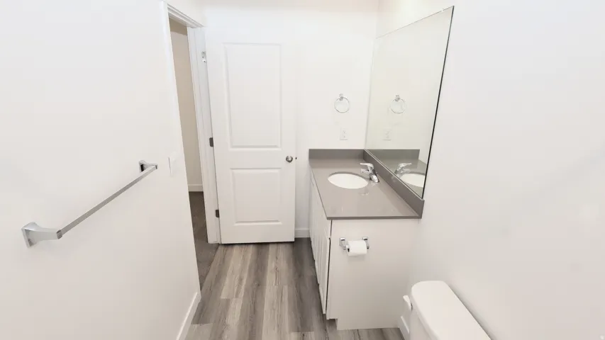 Bathroom featuring wood-finish flooring, a white vanity with a gray countertop, an undermount sink, a large wall-mounted mirror, and white paneled doors