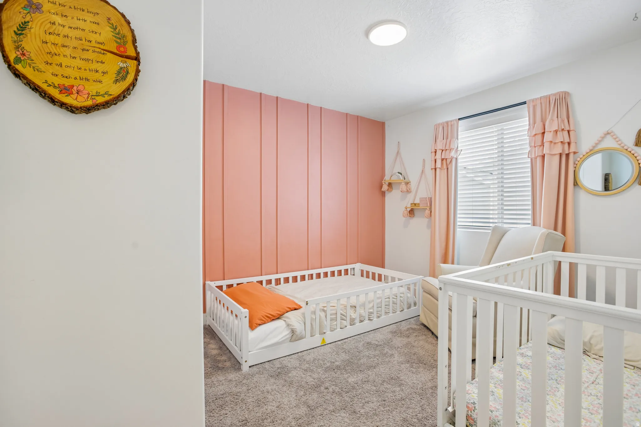Bedroom featuring a coral accent wall with vertical paneling, light gray carpeting, and a white ceiling with a flush-mount light fixture