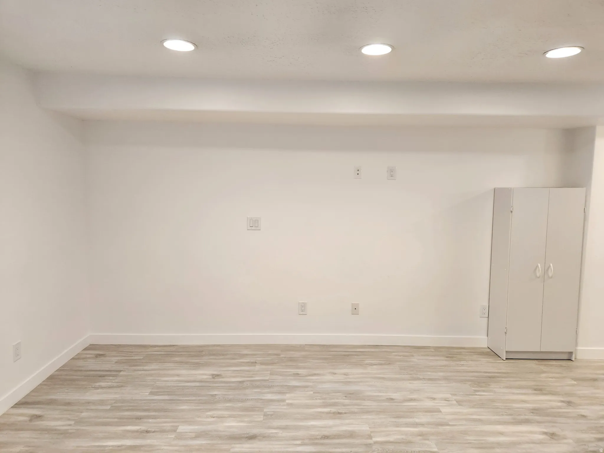 Spacious room featuring light wood-finish flooring, recessed ceiling lighting, and a neutral white color palette