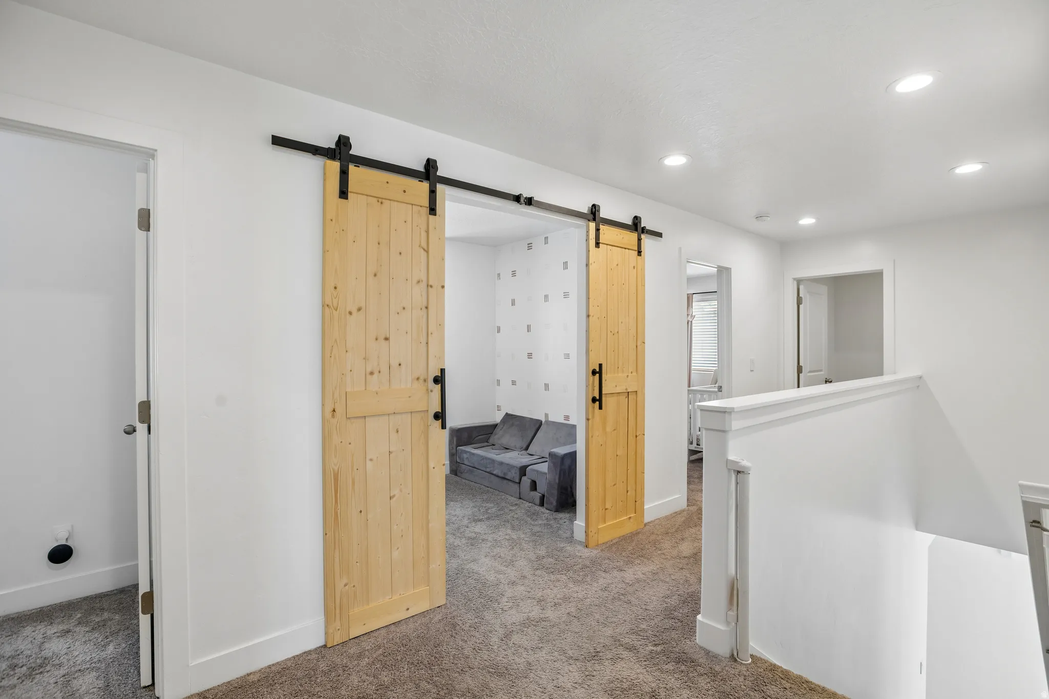 Hallway featuring two natural wood barn doors with black hardware, recessed ceiling lighting, and gray carpet flooring