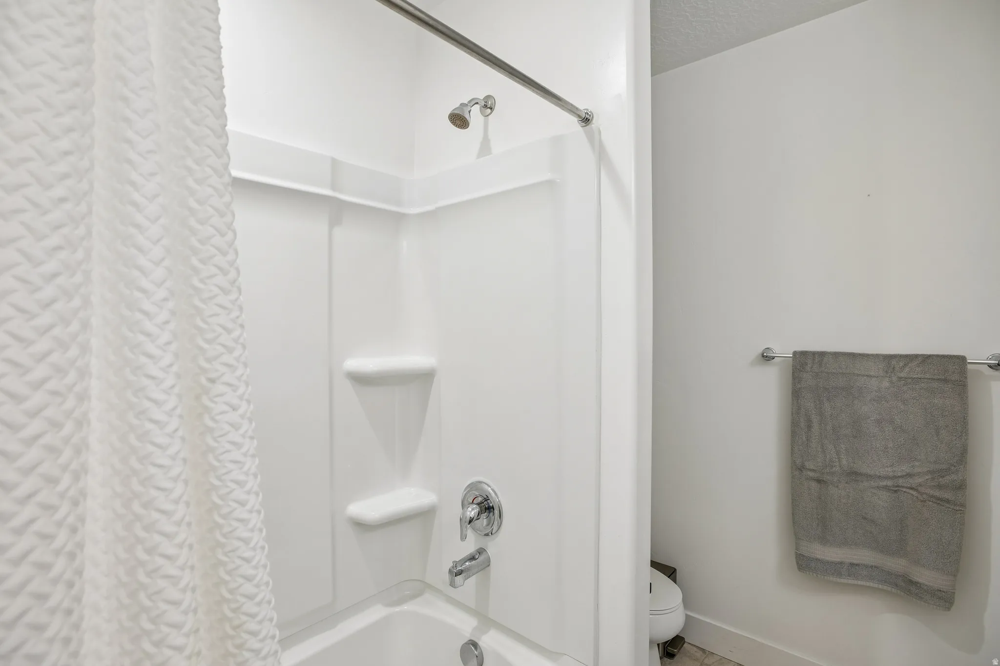 Bathtub with white surround, chrome fixtures, and integrated shelving
