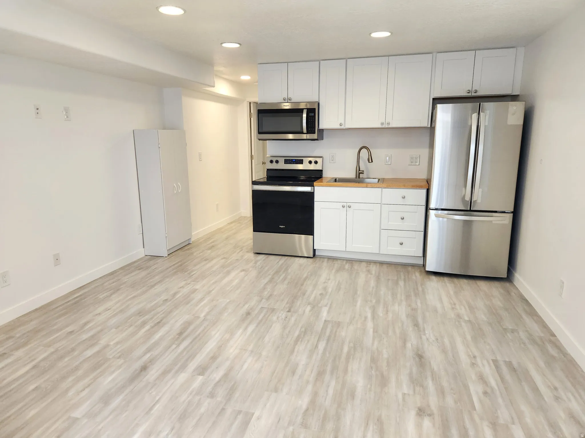 Open-concept space featuring a complete kitchen with stainless steel appliances, white cabinetry, and wood-finish countertops