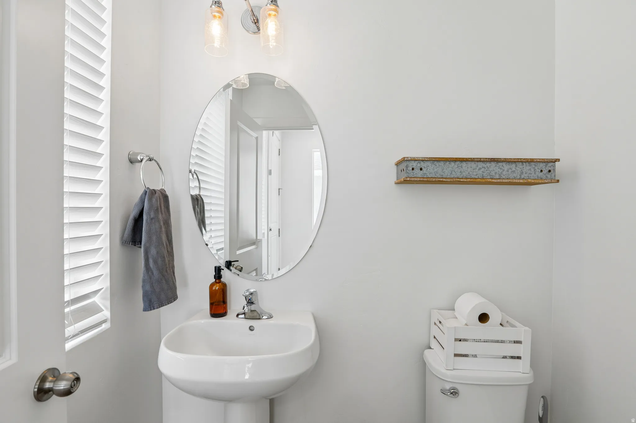 Pedestal sink with chrome faucet, an oval mirror, and wall-mounted light fixture