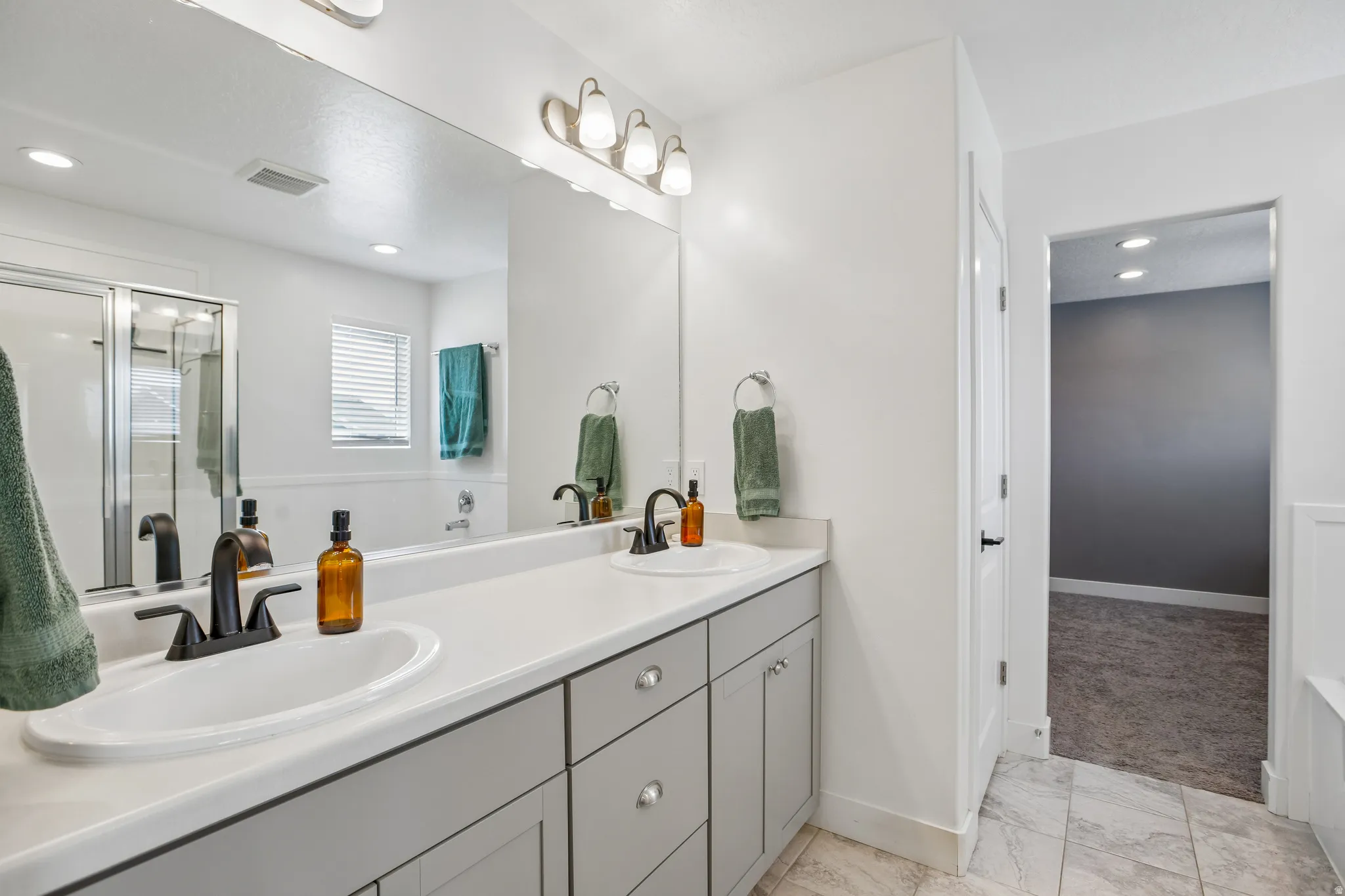 Dual sink vanity with matte black hardware, framed by a large mirror and overhead lighting