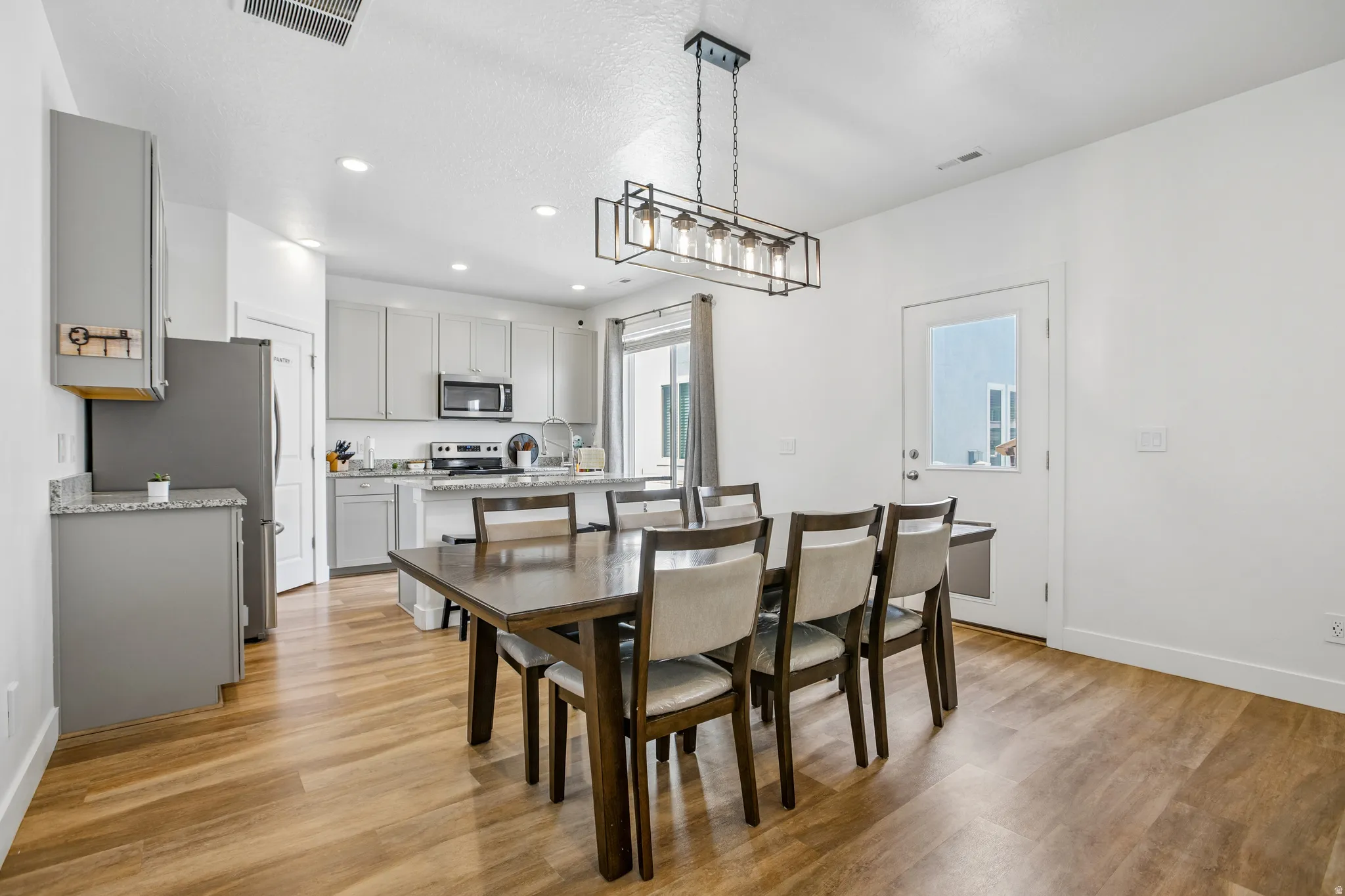 Open-concept kitchen and dining area featuring wood-finish flooring, recessed lighting, and a modern linear chandelier