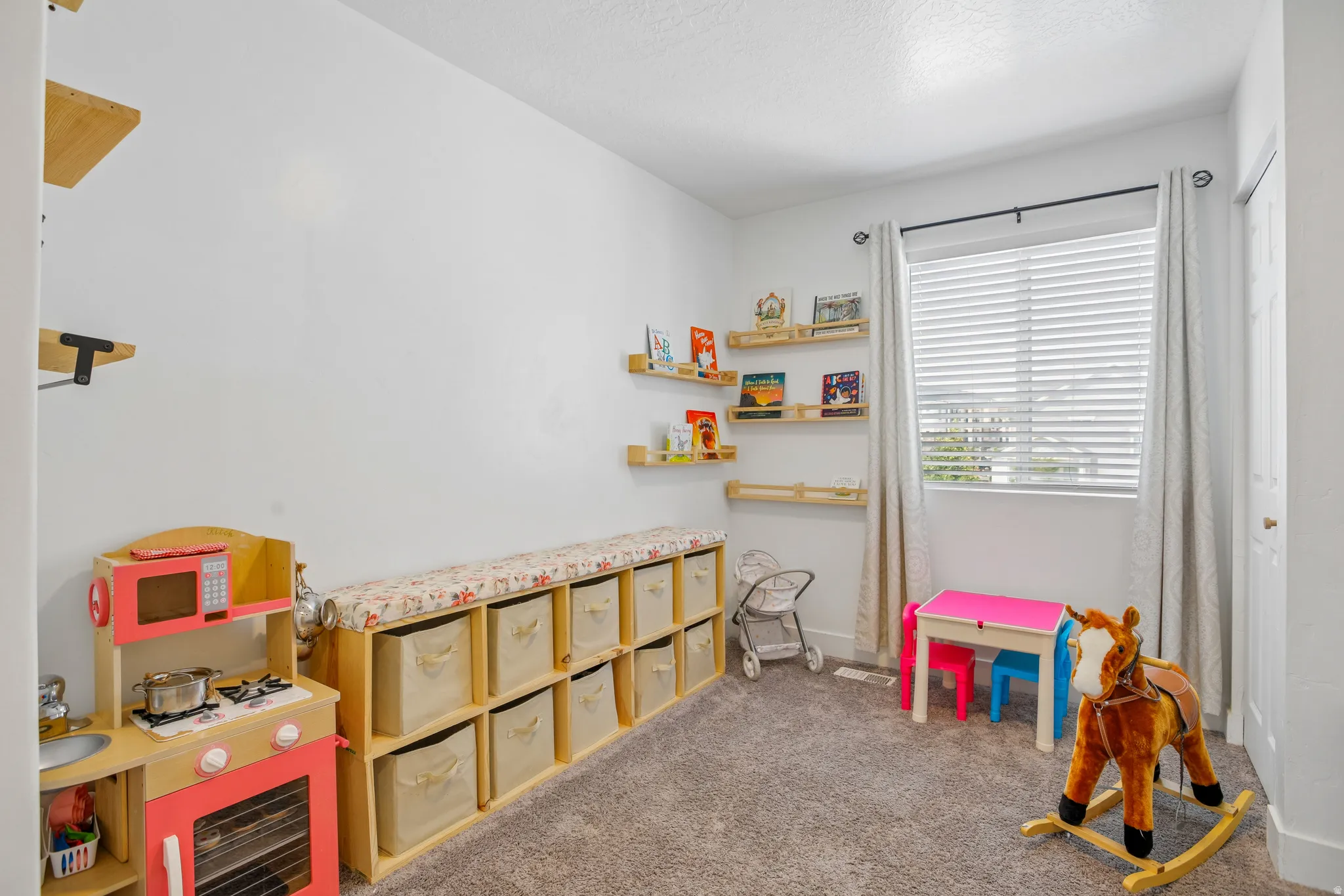 Carpeted room featuring a window with blinds, white walls, and built-in floating wooden shelves