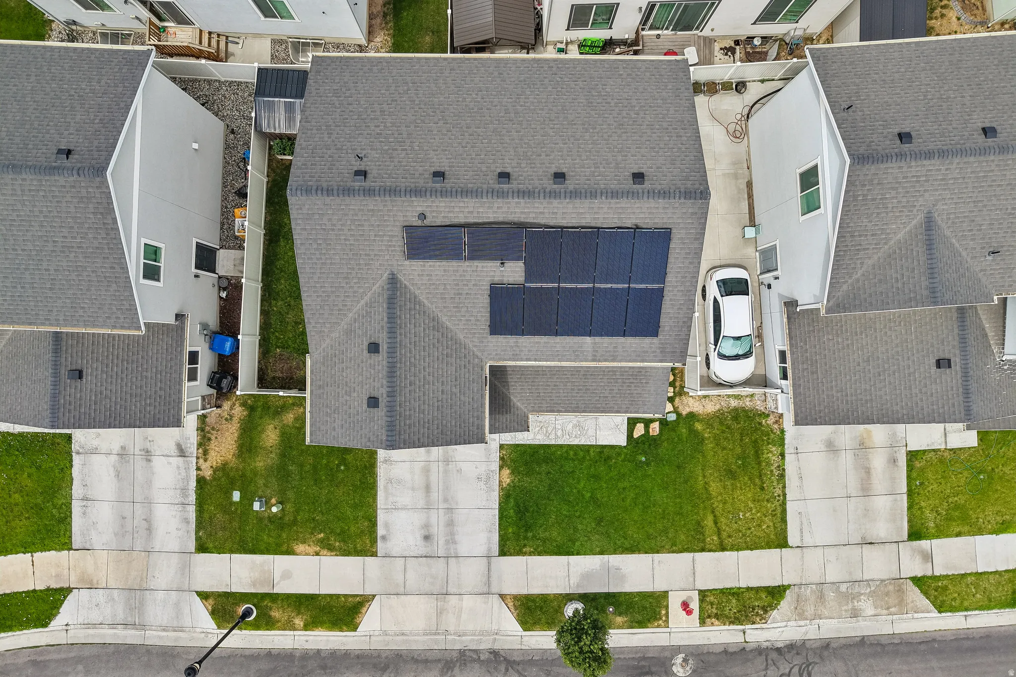 Overhead view showcasing a property with solar panels, a gray shingle roof, green lawn, and concrete driveway