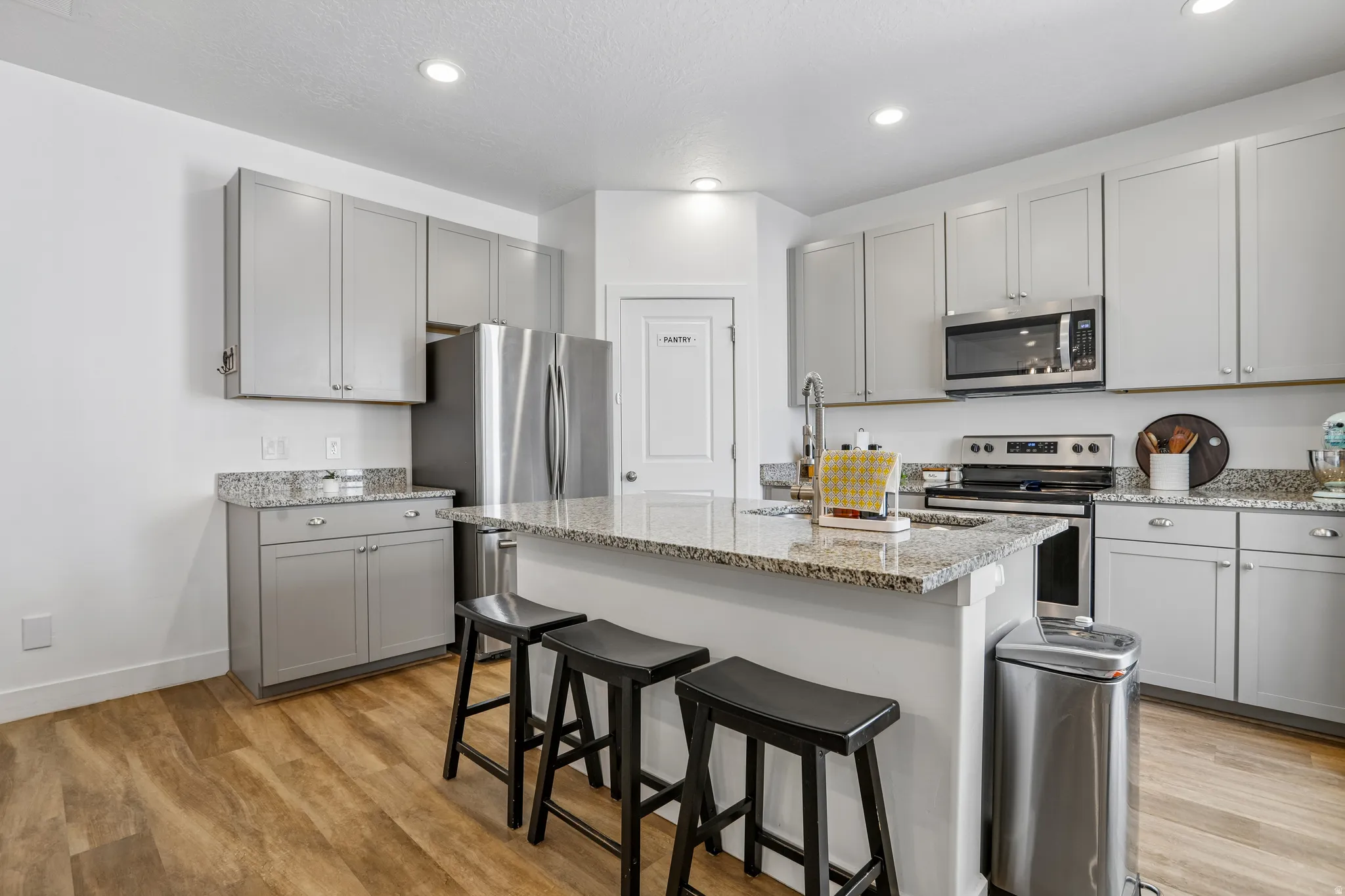 Kitchen featuring an island with stone countertops, gray cabinetry, stainless steel appliances, and wood-finish flooring