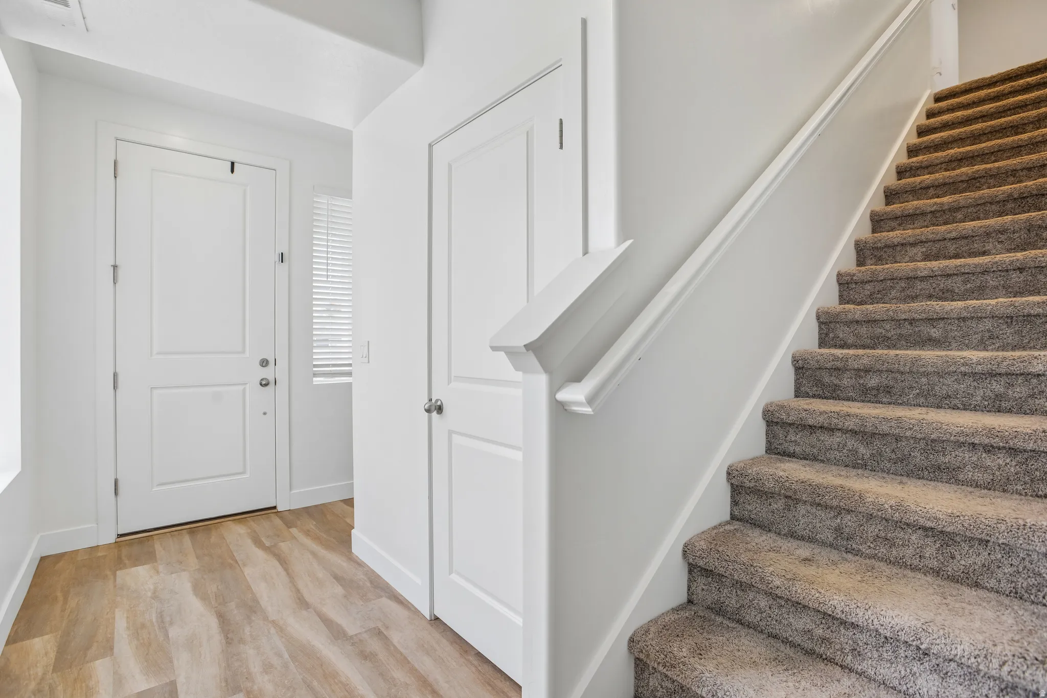 Entryway featuring wood-finish flooring, a two-panel door, and a carpeted staircase with a white handrail