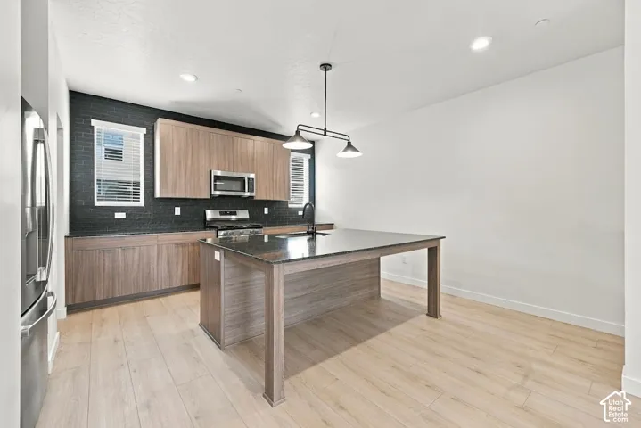 Kitchen featuring a central island with a stone countertop, wood-finish cabinetry, a black brick-patterned backsplash, wood-finish flooring, and a modern industrial-style pendant light fixture